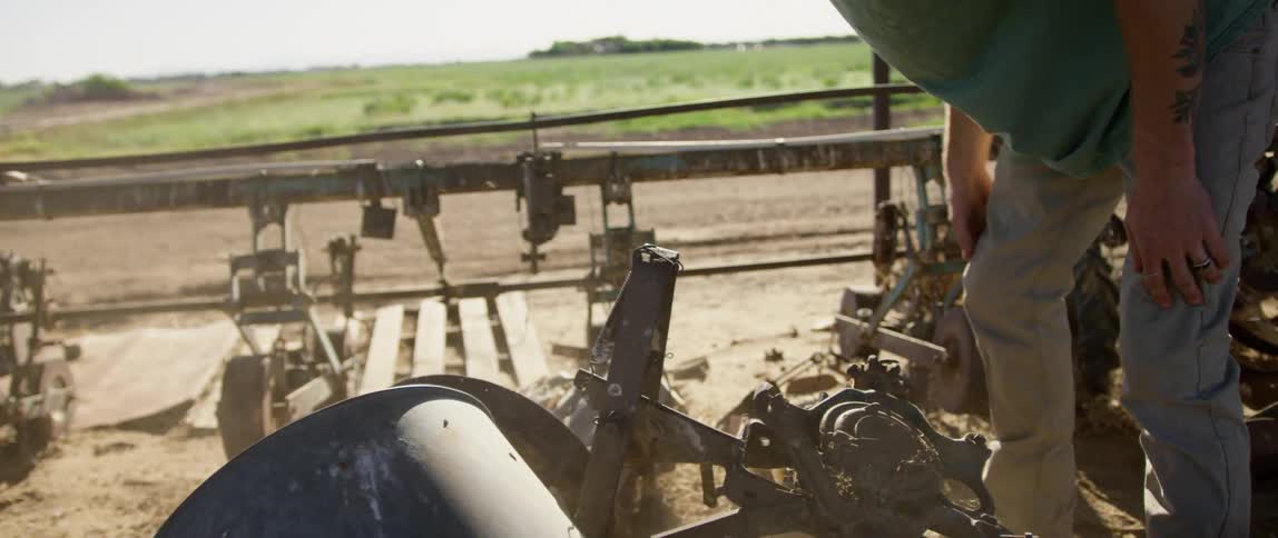 A man works with a piece of machinery outside on a rural land