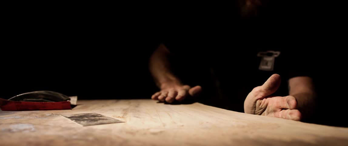 A white man stands the top of a wooden table