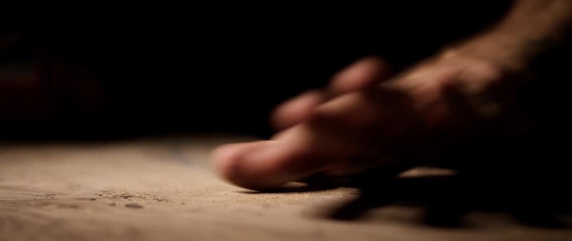 Man with a tattoo on his arm wipes his hand across a wooden surface