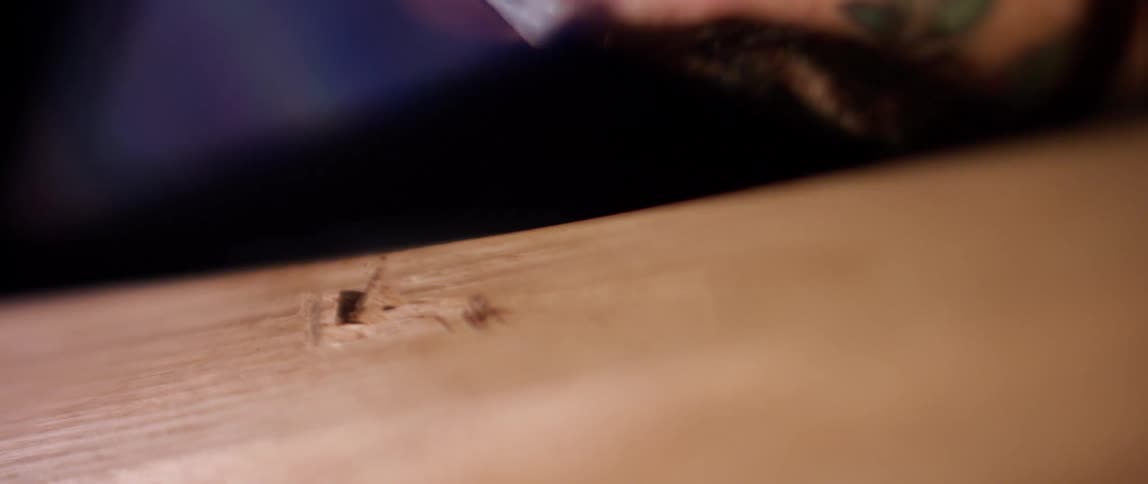 Man uses too to shave off pieces of wood from a plank