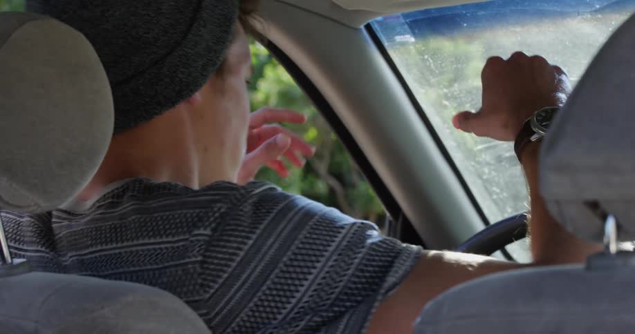 A teenage male sits in the drivers seat of a vehicle and angrily hits the steering wheel