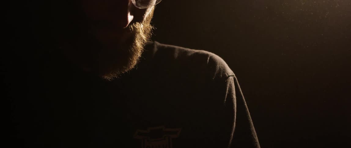 A white man stands quietly in a dark room