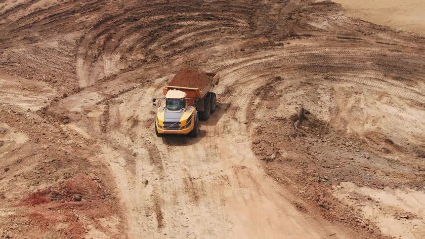 A dump truck loaded with dirt drives off leaving an empty truck behind