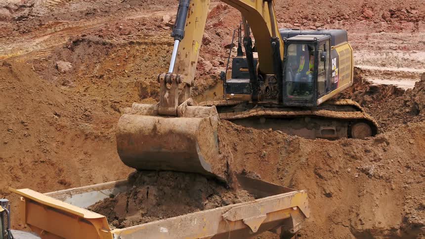 A bull dozer dumps dirt in to the back of a dump truck