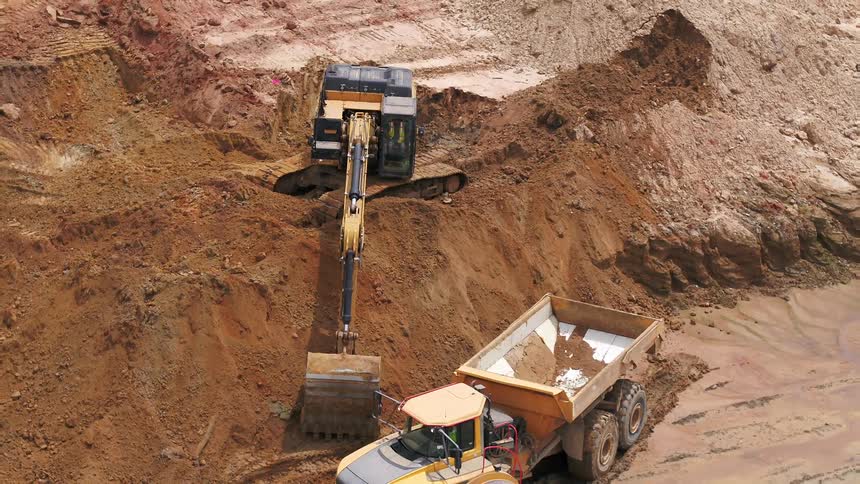 Backhoe digger digs into the dirt while a truck with a bin sits nearby