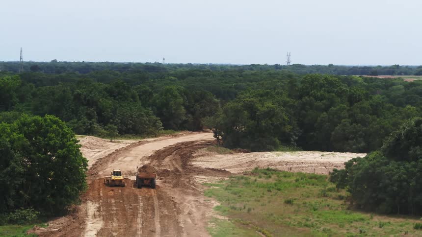 Construction trucks clear land in a forested area