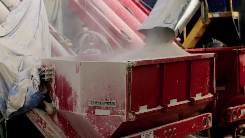 Sand pours down a chute into a red dumpster causing dust to into the air at a construction site