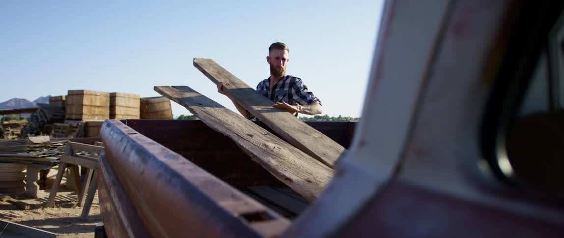 Man loads planks of wood on the bed of a truck