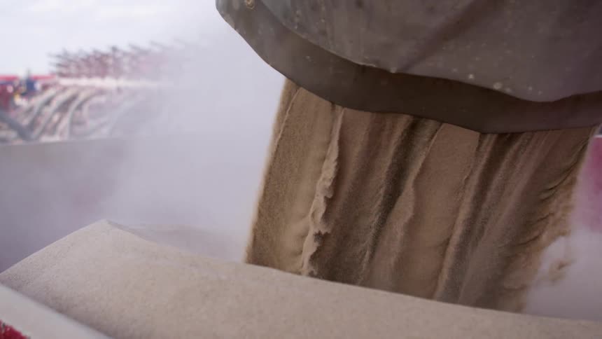Sand pours into a large bin and kicks off clouds of dust