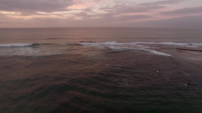 People are surfing at sunset near a pier