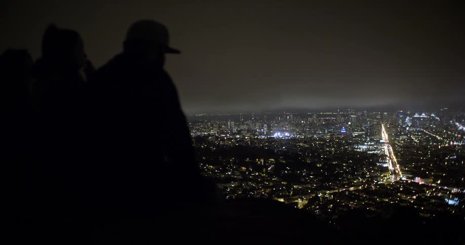 People sitting on a lookout looking at city lights at night
