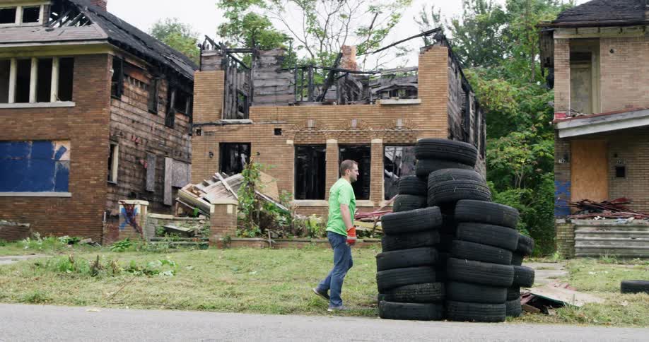 Man piles up used tires on the driveway in front of abandoned houses