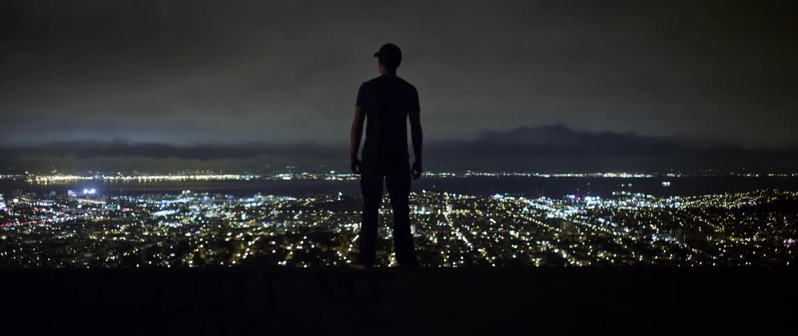 A man is outside at night looking at the city skyline
