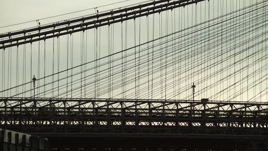 Pedestrians and vehicular traffic crossing a suspension bridge at sunrise
