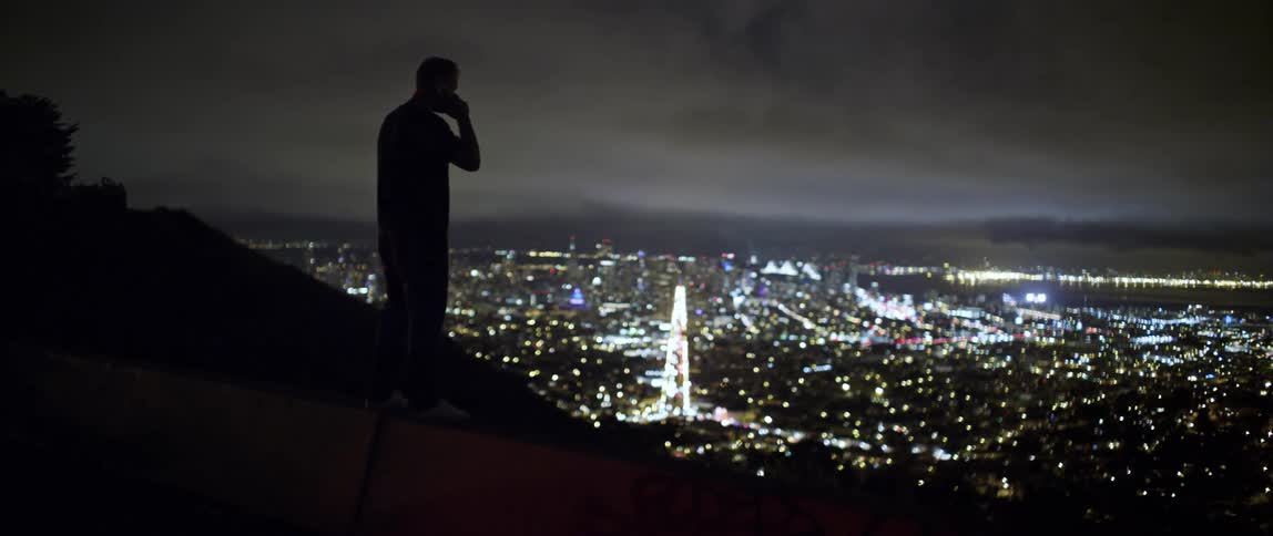 A man talking on his phone looks at the lit up city skyline