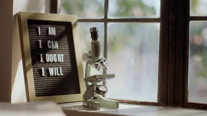 Microscope and sign with words on it sit on window sill