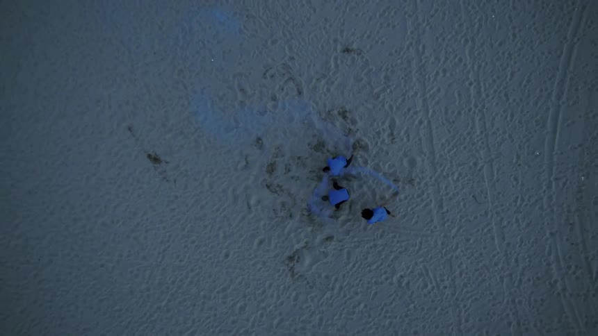 Birds eye view of teenagers spinning around in the sand and releasing blue dye