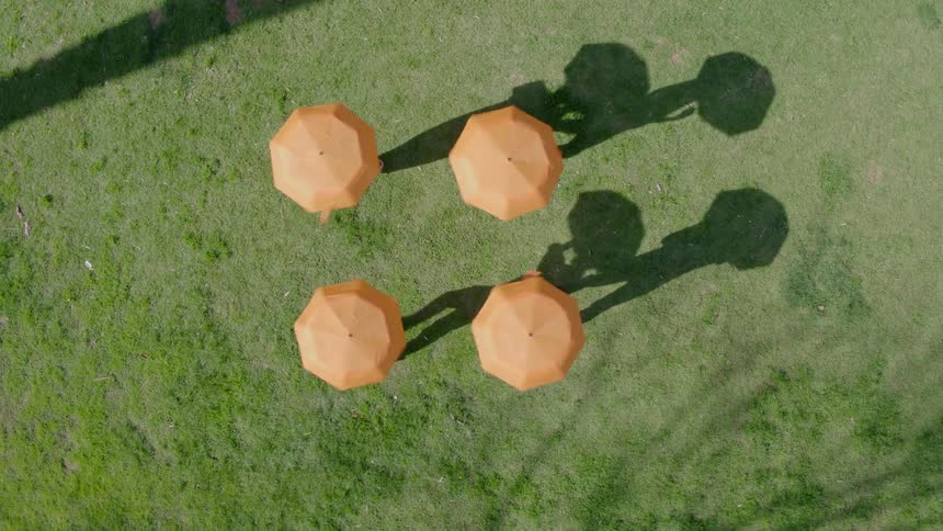 Four people walk in a circle while spinning umbrellas above their heads