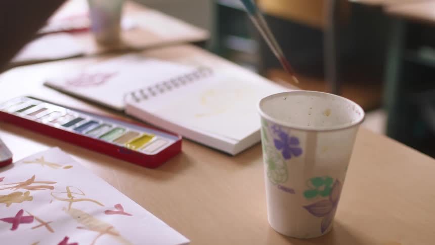 A child dips a paintbrush in a cup of water
