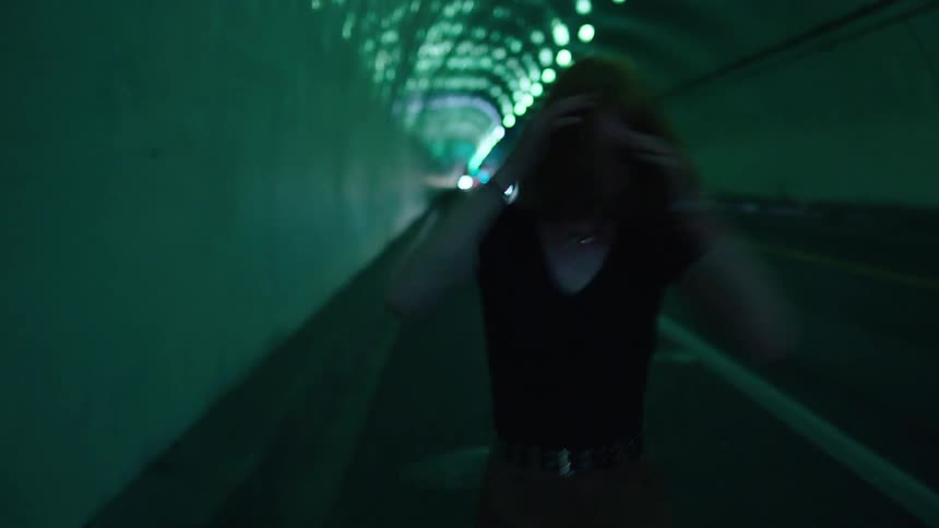 Time lapse of a teen walking through a tunnel and running her hands through her hair and throwing herself against a wall