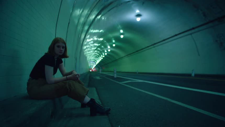 Time lapse of a sad looking teenager sitting in a tunnel as cars drive by