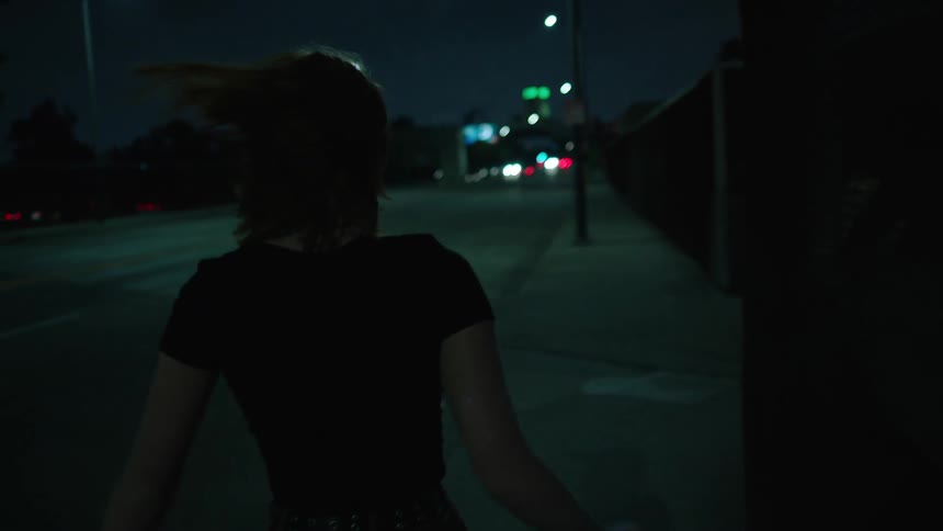 Girl dances and skips along barrier on bridge passing over highway at night