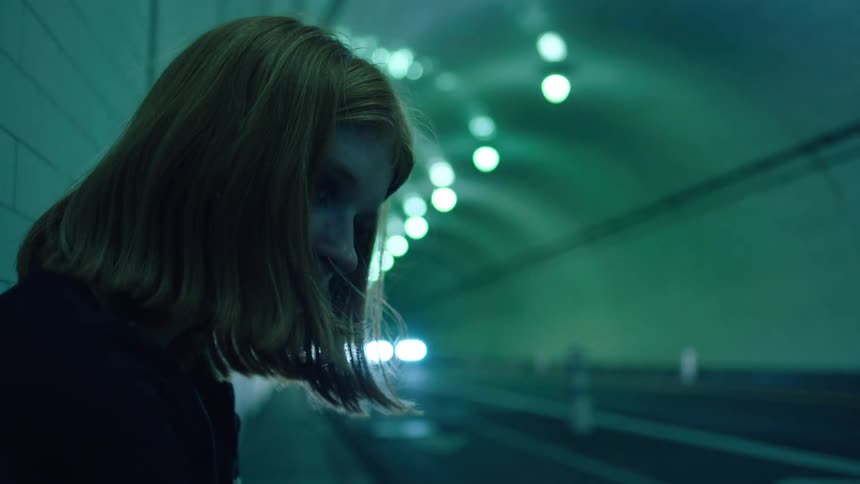 Woman waits on sidewalk near side of tunnel as traffic flows to and fro