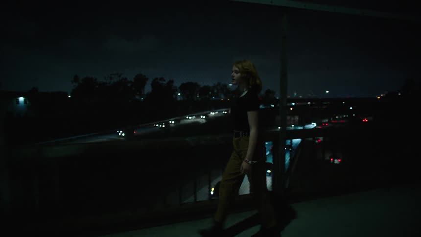 Woman walking happily and touching wire fences crosses an overpass over busy roads at night
