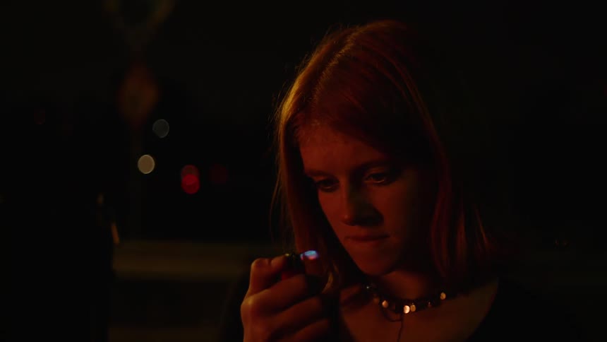 Young woman plays with a lighter at night in the street