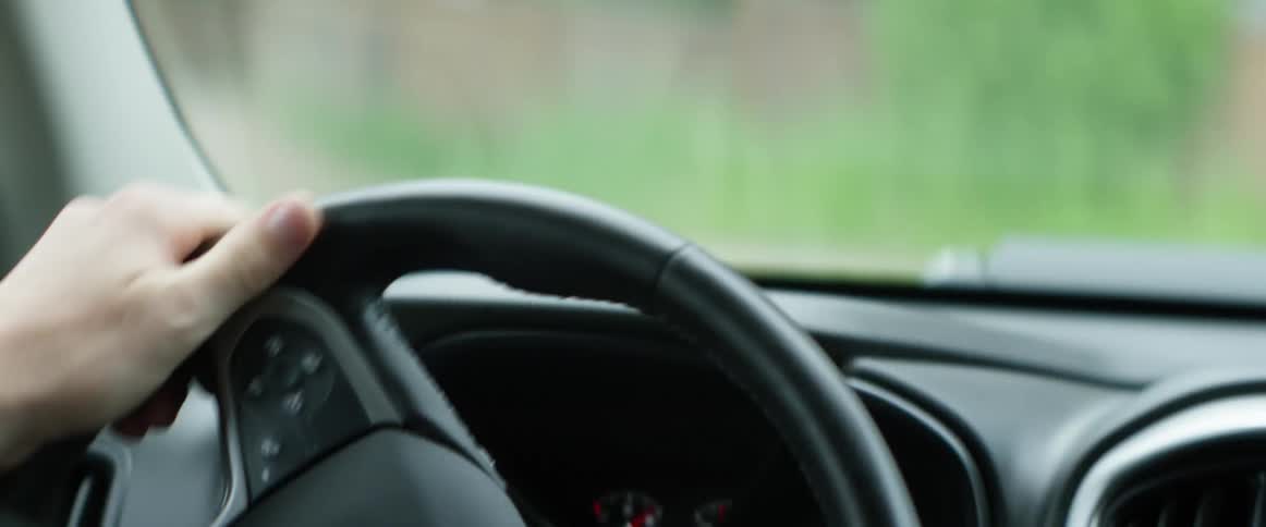 Driver with a shirt and bracelet turns the steering wheel in a car