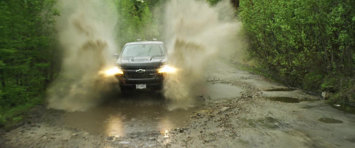 A vehicle driving on a remote road splashing up a big puddle
