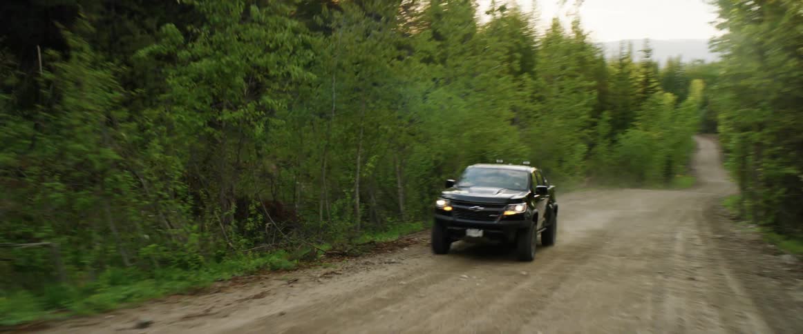 A truck driving down a dirt road with forest on either side
