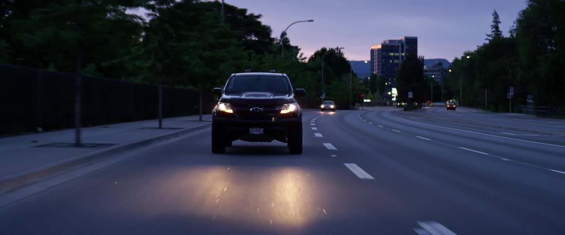 Cars with their headlights on travel on the city highway near the trees
