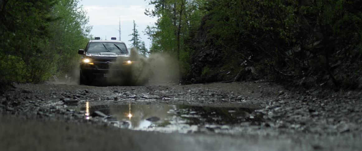 A truck drives through a large puddle on a gravel off road area