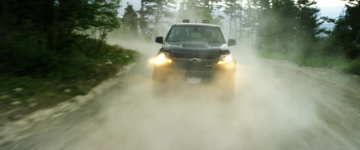A vehicle being driven very fast down a dirt road next to a forest