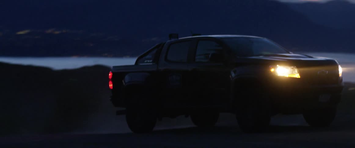 Pickup truck with headlights illuminating a road drives uphill at dusk