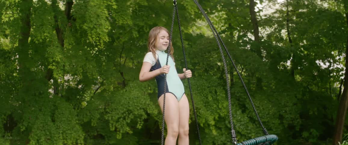 A young girl stands on a swing in a forest