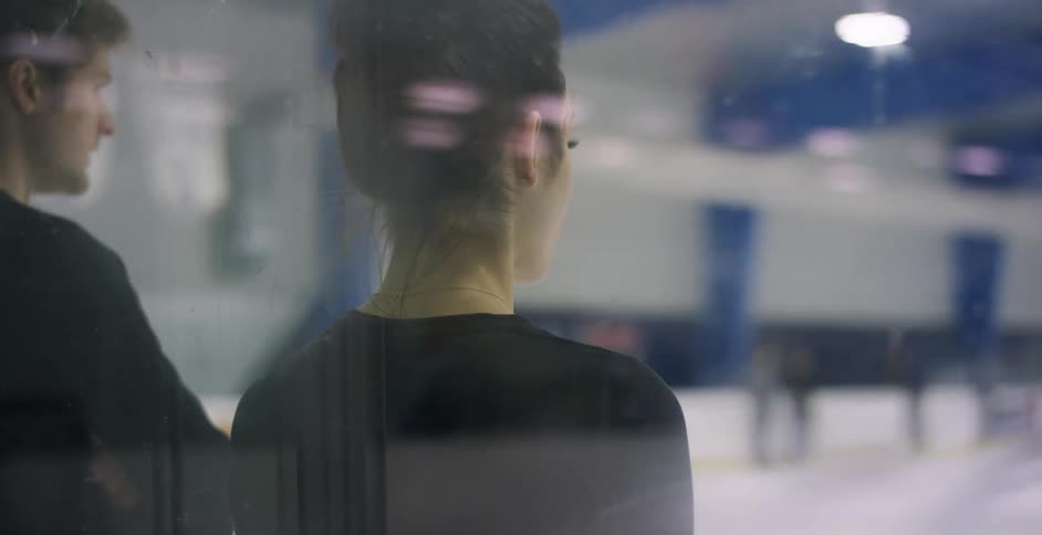 Man and woman stand at the end of an ice rink as they look across it