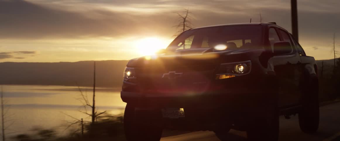 Truck driving on road along side a lake at sunset
