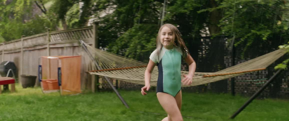 A young girl runs around a sprinkler in her backyard