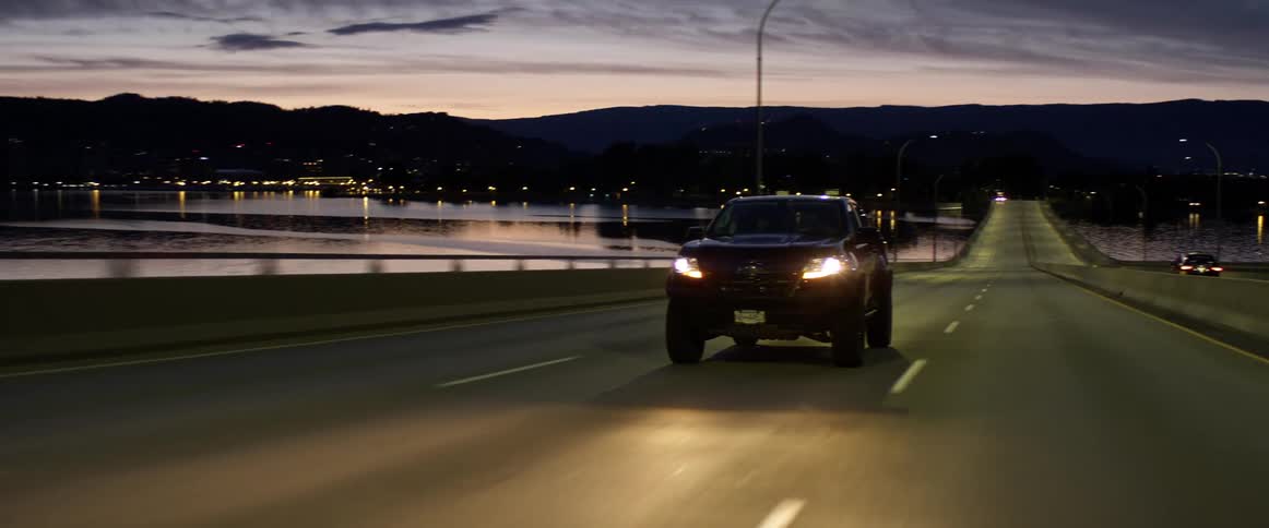 Pickup truck illuminating the road with headlights crosses the bridge at dusk