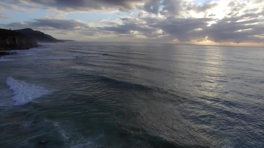 Flowing ocean waters under a cloudy sky at sunset