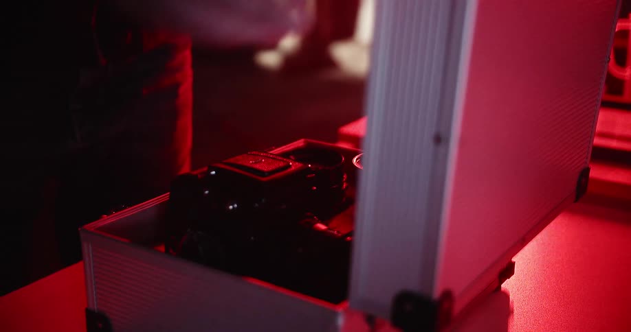 A man in a photographers dark room places a camera into a camera case and close it