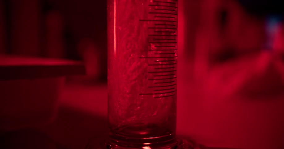 Liquor is poured in a lined glass in a living room lit with a red light