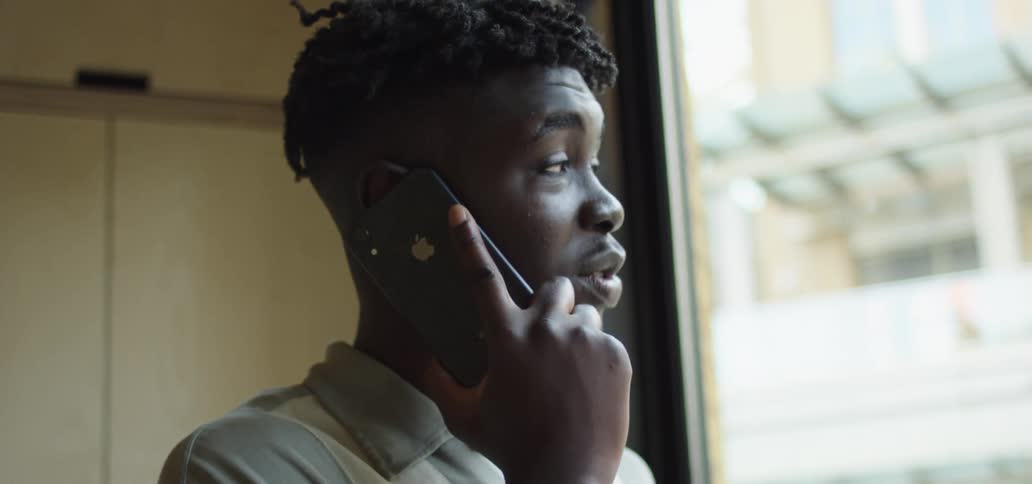 Black man with a grey polo shirt talks on a smartphone and smiles slightly
