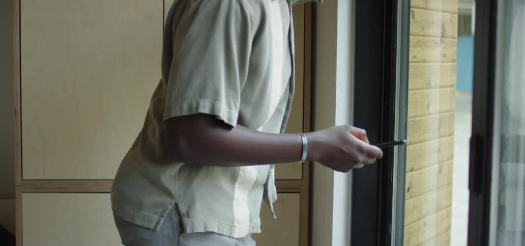 A teenager looks out his window as he scrolls on his cell phone