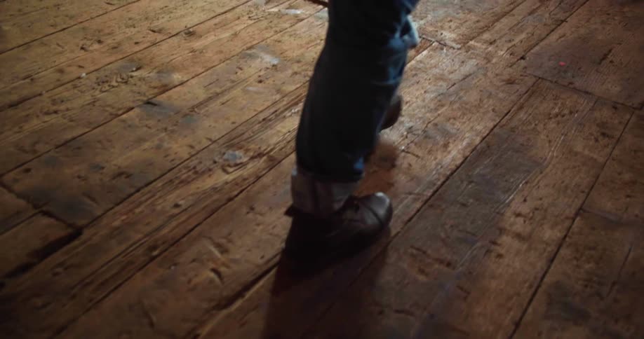 Man with brown boots and jeans walks on a wood floor