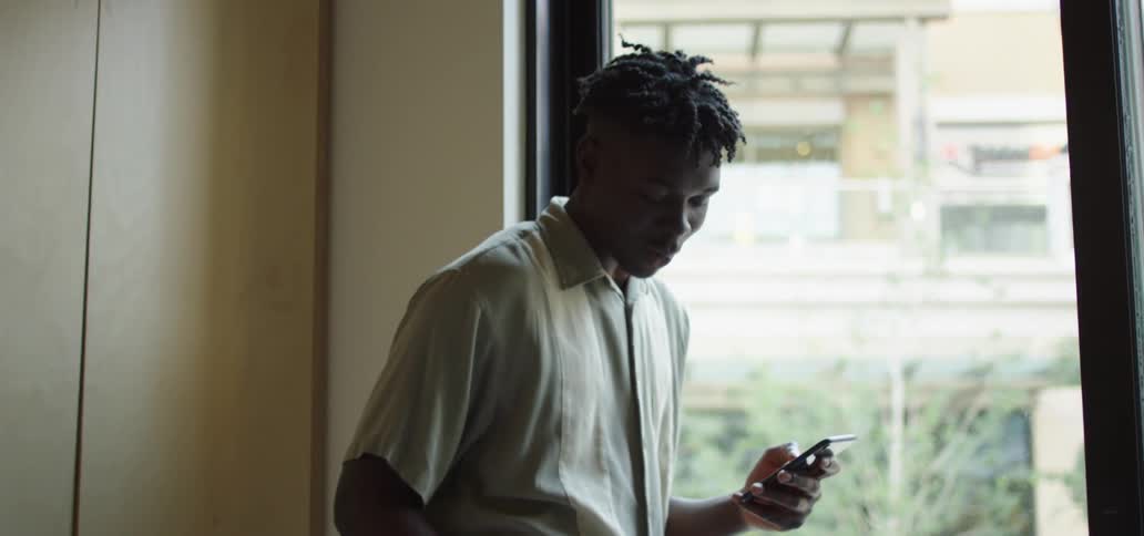 A teenager stands inside and talks on his cell phone