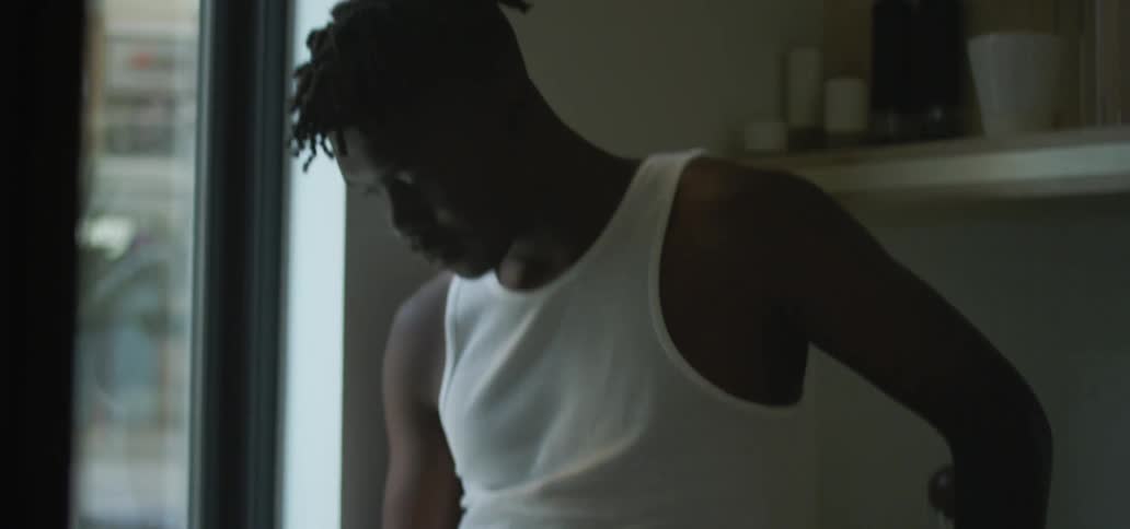 Male leaning against the kitchen counter next to a window takes a sip of a drink from a cup while reading a magazine and then puts the cup on the counter beside him