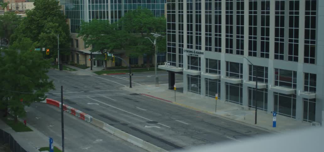 Black man with a grey polo shirt and blue face mask looks at the empty street from the top of a building during lockdown